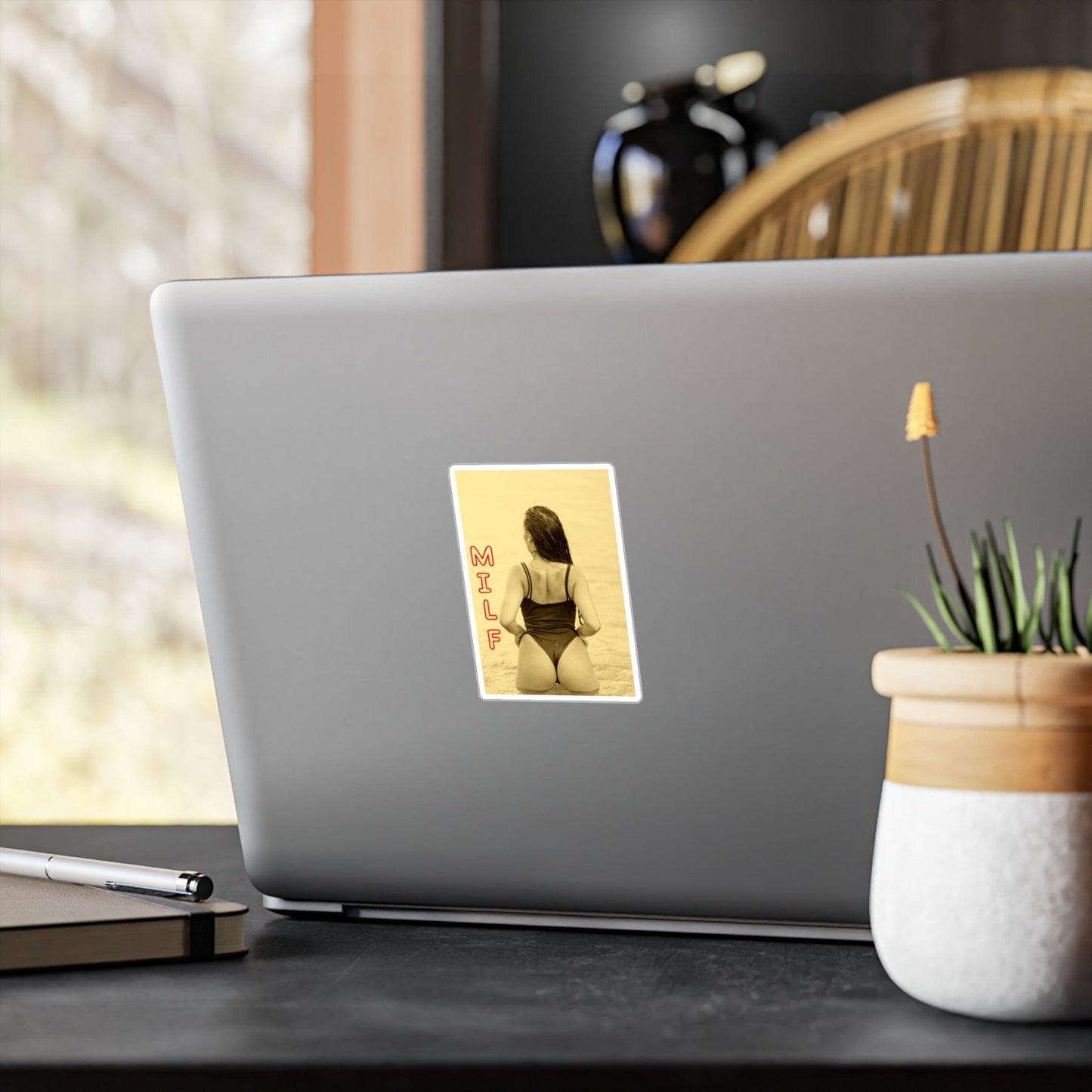 Laptop with a sticker on a desk next to a plant and pen