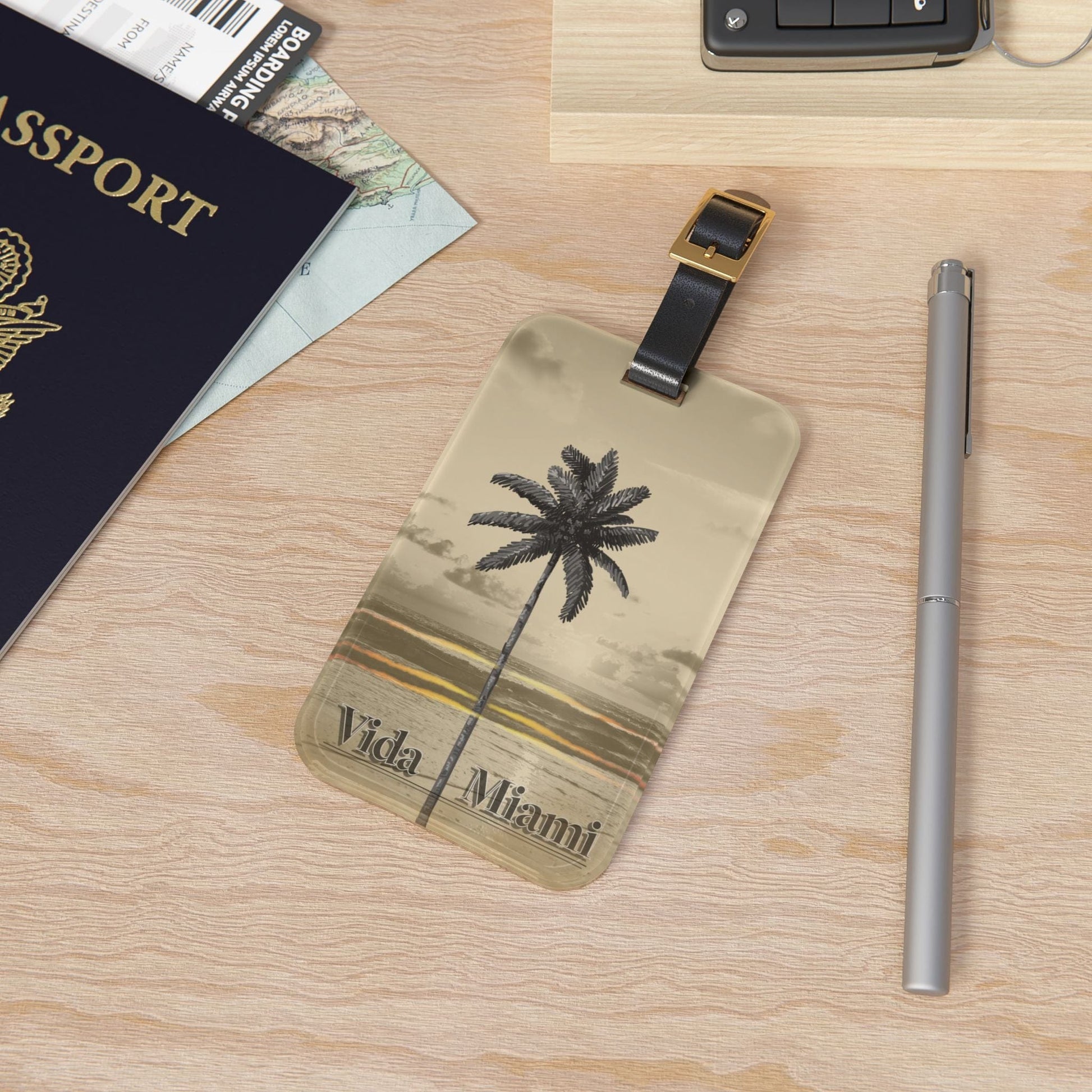 Luggage tag with palm tree design and 'Vida Miami' text on a wooden surface with passport and pen.