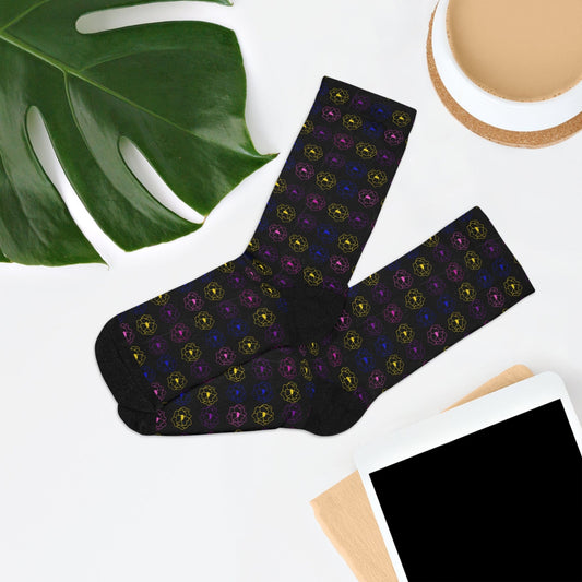Black socks with colorful pattern on a white surface with a plant and cup in the background